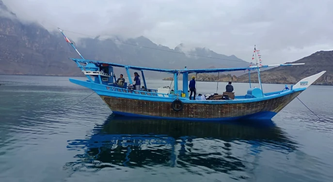 Traditional dhow anchored on calm water beneath cloudy Musandam mountains