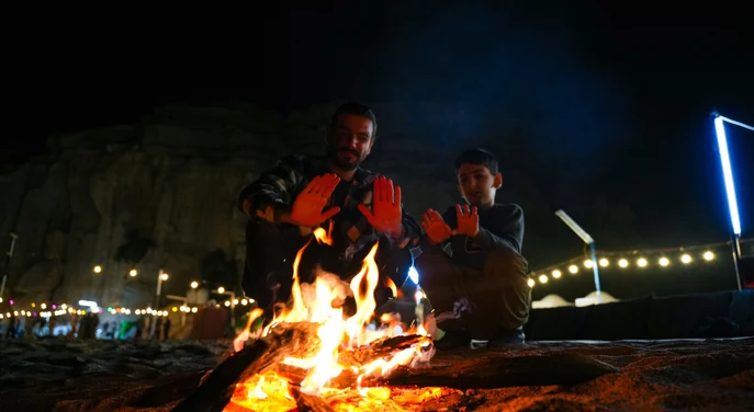 Guest and child warming their hands beside a campfire at a Musandam beach camp