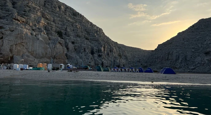 Remote Musandam beach campsite beneath rocky mountains at sunset