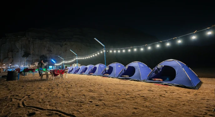 Wide night view of tents and string lights at a Musandam beach campsite