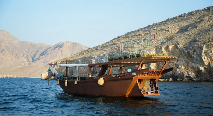 Traditional wooden dhow cruising beside the rocky mountains of Musandam