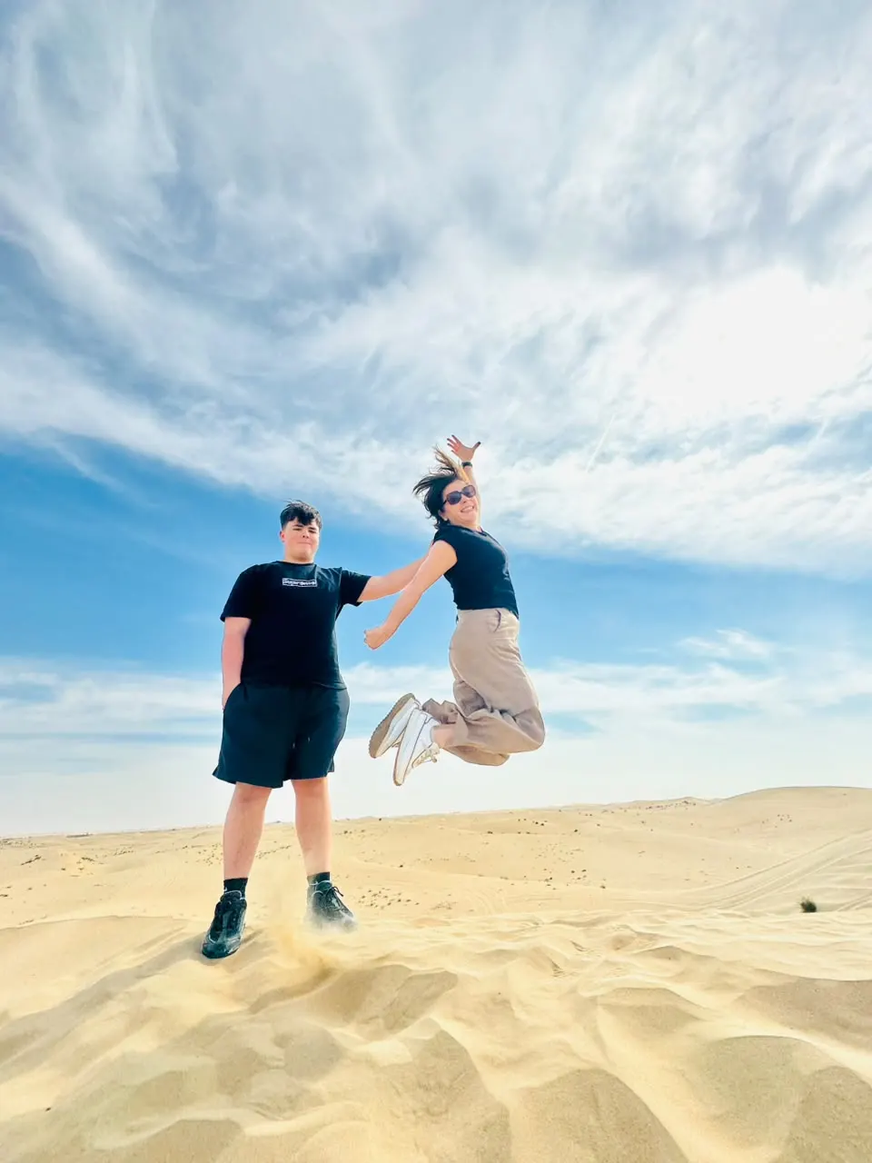 Two guests jumping for a photo on a dune during an Abu Dhabi desert safari
