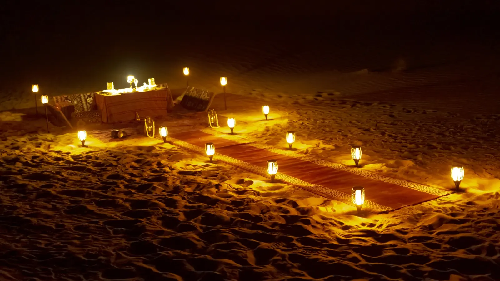 Private dinner setup on the sand lit by lanterns in the Abu Dhabi desert