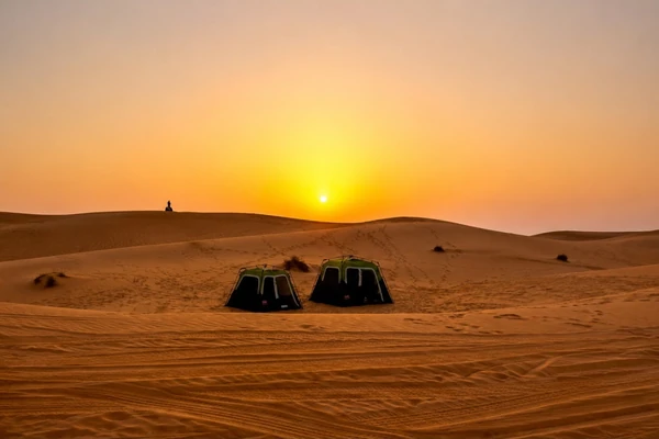 Desert tents set up among dunes at sunset