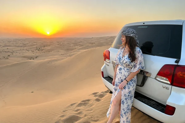 Woman beside a 4x4 watching sunset over Abu Dhabi desert dunes