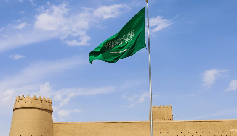 Saudi Arabian flag above a heritage fort for a Saudi visa for UAE residents guide