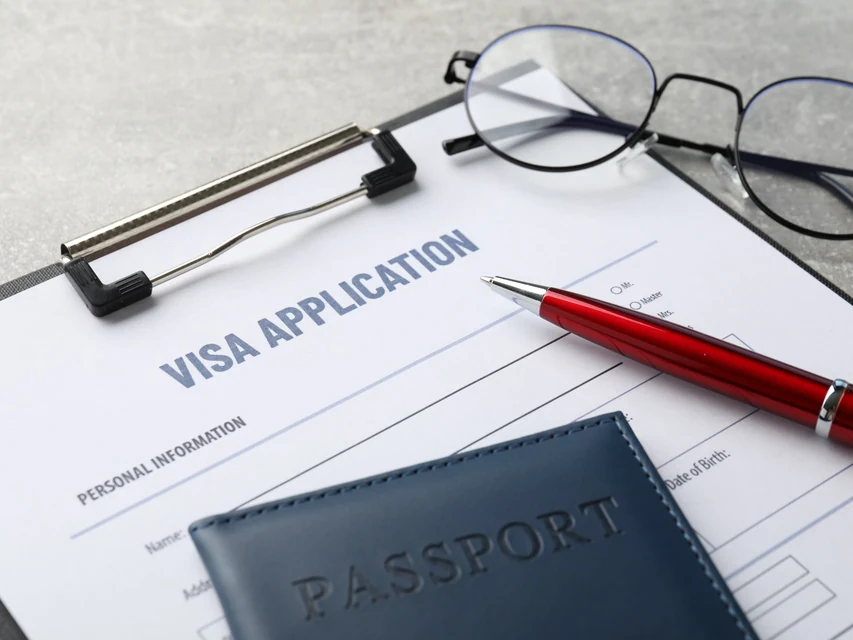 Visa application form with passport, pen and glasses illustrating New Zealand Visitor Visa applications